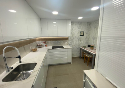 Cocina DiGiovanni, Reforma, Zaragoza, cocina, Mueble a medida, cocina moderna, cocina blanca, blanco y marmol, taburete alto, barra, mesa alta, Porcelanosa, tirador oculto, amueblamiento, Silestone, Dekton, Consentino, encimera crema, campana oculta, barra desayuno, Balay, Bosch, cemento, reloj cocina, mueble auxiliar, electrodomesticos negros,, horno cristal negro, microondas cristal negro, frigorifico acero, cocina, suelo crema, decorativo, cocina alargada, baldosa blanca, mueble microondas, taburete rojo, cocina azul, turquesa, mueble caldera, decorativo, encimera granito negro, tira led, luz led, mueble blanco, electrodomésticos cristal blanco, encimera marmol blanco, frontal blanco y madera, papel pintado