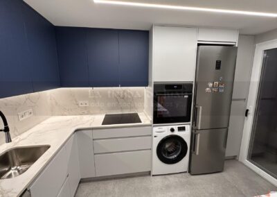 Cocina DiGiovanni, Reforma, Zaragoza, cocina, Mueble a medida, cocina moderna, cocina blanca y negra, taburete madera, Porcelanosa, Saloni, tirador oculto negro, amueblamiento, Silestone, Dekton, Consentino, encimera negra, campana decorativa cristal negro, Balay, Bosch, reloj cocina, mueble auxiliar, electrodomesticos negros, horno cristal negro, microondas cristal negro, frigorifico acero, cocina, suelo gris, decorativo, cocina alargada, baldosa blanca, mueble microondas, decorativo, tira led, luz led, mueble blanco, frontal, mueble madera y blanco, mueble blanco, electrodomesticos acero, mueble blanco, campana decorativa negra, columna horno microondas, frigorífico cajones, pared pizarra, mueble azul mate