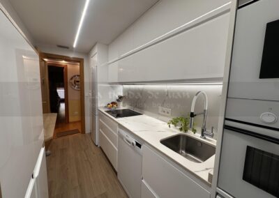 Cocina DiGiovanni, Reforma, Zaragoza, cocina, Mueble a medida, cocina moderna, cocina blanca y negra, taburete madera, Porcelanosa, Saloni, tirador oculto negro, amueblamiento, Silestone, Dekton, Consentino, encimera negra, campana decorativa cristal negro, Balay, Bosch, reloj cocina, mueble auxiliar, electrodomesticos negros, horno cristal negro, microondas cristal negro, frigorifico acero, cocina, suelo gris, decorativo, cocina alargada, baldosa blanca, mueble microondas, decorativo, tira led, luz led, mueble blanco, frontal, mueble madera y blanco, mueble blanco, electrodomesticos acero, mueble blanco, campana decorativa negra, columna horno microondas, frigorífico cajones, pared pizarra, mueble azul mate