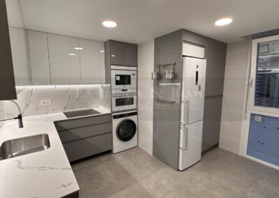 Cocina DiGiovanni, Reforma, Zaragoza, cocina, Mueble a medida, cocina moderna, cocina blanca y negra, taburete madera, Porcelanosa, Saloni, tirador oculto negro, amueblamiento, Silestone, Dekton, Consentino, encimera negra, campana decorativa cristal negro, Balay, Bosch, reloj cocina, mueble auxiliar, electrodomesticos negros, horno cristal negro, microondas cristal negro, frigorifico acero, cocina, suelo gris, decorativo, cocina alargada, baldosa blanca, mueble microondas, decorativo, tira led, luz led, mueble blanco, frontal, mueble madera y blanco, mueble blanco, electrodomesticos acero, mueble blanco, campana decorativa negra, columna horno microondas, frigorífico cajones, pared pizarra, mueble azul mate