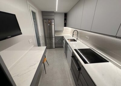 Cocina DiGiovanni, Reforma, Zaragoza, cocina, Mueble a medida, cocina moderna, cocina blanca y negra, taburete madera, Porcelanosa, Saloni, tirador oculto negro, amueblamiento, Silestone, Dekton, Consentino, encimera negra, campana decorativa cristal negro, Balay, Bosch, reloj cocina, mueble auxiliar, electrodomesticos negros, horno cristal negro, microondas cristal negro, frigorifico acero, cocina, suelo gris, decorativo, cocina alargada, baldosa blanca, mueble microondas, decorativo, tira led, luz led, mueble blanco, frontal, mueble madera y blanco, mueble blanco, electrodomesticos acero, mueble blanco, campana decorativa negra, columna horno microondas, frigorífico cajones, pared pizarra, mueble azul mate